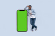 © FOTO_STOCKER - Excited black man standing and pointing Big smartphone with blank green screen, demonstrating copy space for app or website design, standing over blue studio background, mockup image