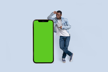Excited black man standing and pointing Big smartphone with blank green screen, demonstrating copy space for app or website design, standing over blue studio background, mockup image