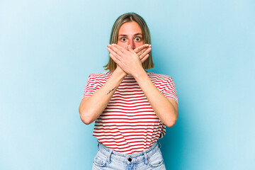 Wall Mural - Young caucasian woman isolated on blue background shocked covering mouth with hands.