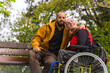 © unai - A person with a disability young man in a wheelchair with a friend on a bench in a public park in the city