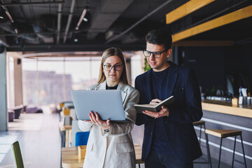 Wall Mural - Beautiful european business woman and business man looking at the screen of a laptop computer and talking to a businessman in the office.