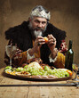 Its good to be the king. A mature king feasting alone in a banquet hall.