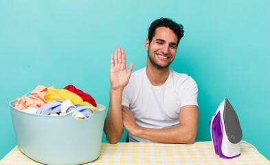 hispanic handsome man smiling happily, waving hand, welcoming and greeting you iron and clothes concept