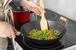 Woman cooking tasty vegetable mix in wok pan at home, closeup