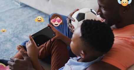 Poster - Animation of emoticons over african american father and son using smartphone with copy space