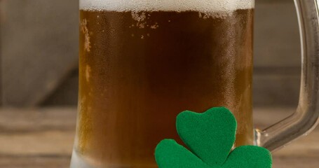 Sticker - Animation of clover leaf leaning on glass of beer in background