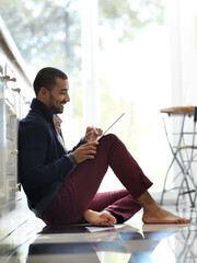 Aufkleber - Theres always time for social media. Shot of a smiling young man sitting on his kitchen floor using a digital tablet.