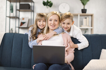 Wall Mural - Happy young caucasian mother relax on comfortable couch with little kids have fun watch video on laptop together, charming family rest on sofa in living room using computer with children