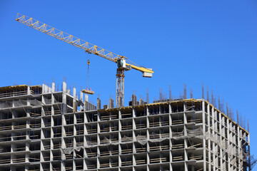 Wall Mural - Construction tower crane above unfinished residential building on blue sky background. Housing construction, apartment or office block