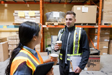 Worker With Hot Drink, Talking To Colleague In Distribution Warehouse