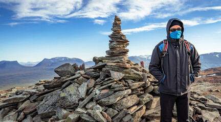 Wall Mural - Male hiker standing on the top of Nuolja, or Njulla, mountain in Abisko National Park in arctic Sweden. Lapponian gate, or Lapporten, in the back. Adventure in remote arctic wilderness.