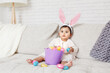 © anoushkatoronto - Cute Indian baby girl with pink bunny ears and basket of colorful eggs celebrating Easter holiday.