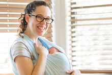 Happy Young Mother Holding Her Sleeping Newborn Baby In A Wrap Sling