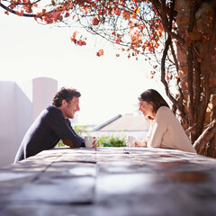 Wall Mural - Sharing stories in the sunlight. A couple seated at a wooden table beneath the autumn leaves.