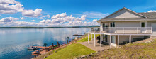 Panoramic View Of A Beautiful, Large Modern Luxury Summer Holiday Home, Featuring Sun Decks, Glass Railings, And Large Windows, Set Beside A Small Lake In Central British Columbia, Canada.
