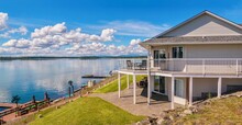 Wide Angle View Of A Beautiful, Large Modern Luxury Summer Holiday Home, Featuring Sun Decks, Glass Railings And Large Windows, Set Beside A Small Lake In Central British Columbia, Canada.