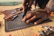 © Wavebreak Media - Cropped hands of african american young craftsman cutting leather with blade on cutting mat