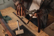 © Wavebreak Media - Midsection of african american young craftsman making hole on leather belt with punch plier