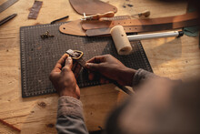 Cropped Hands Of African American Young Craftsman Fixing Buckle On Leather Belt At Workbench