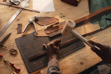 African American Young Craftsman Making Hole On Leather Belt With Hammer And Equipment