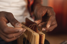 Close-up Of African American Young Craftsman Stitching Leather Wallet With Thread In Workshop