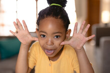 Playful Portrait Of Cute African American Girl Sticking Out Tongue And Gesturing At Home