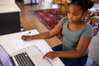 © Wavebreak Media - African american girl using laptop while writing on book during online school at home
