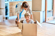 We have liftoff. Shot of a cheerful young woman pushing her son around in a box imagining its a car inside at home during the day.