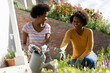 © Wavebreak Media - Happy mother pointing while teenage daughter watering plants in backyard on sunny day