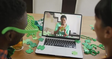 Poster - Smiling african american woman with beer wearing clover shape band on video call on laptop