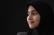 Close up portrait of little Muslim girl wearing black Hijab on black background, looking at side