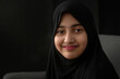 Close up portrait of little Muslim girl wearing black Hijab on black background, smiling at camera