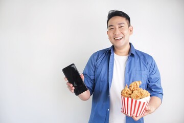 Happy Asian man fried chicken bucket and smartphone standing over white background with copy space.