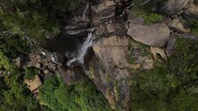 After A Long Walk Over The Edge Of The Higher Lovers Leaf Waterfall Several Tourists Look At The Water That Falls Over The Carved Rocks Between The Nature Of Sri-Lanka. Top Down Drone Lowering Shot