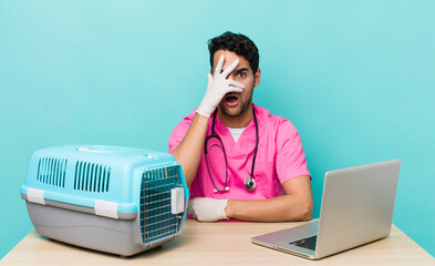 Wall Mural - hispanic handsome man looking shocked, scared or terrified, covering face with hand. veterinarian concept