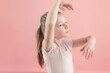 close-up of a little girl in tutu dancing at the ballet school against pink wall