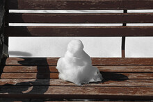 Spring. Small Snowman Is Melting On Wooden Bench