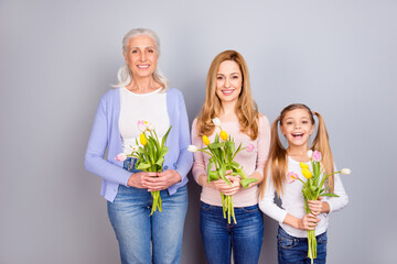 Wall Mural - Portrait of three cheerful idyllic woman hold fresh flowers toothy smile isolated on grey color background