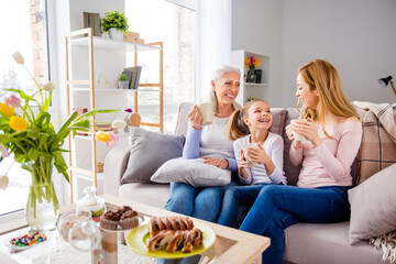 Wall Mural - Photo of three cheerful peaceful people enjoy hot tea mug sitting couch communicate indoors