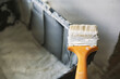 © Dzmitry - a paint brush with a yellow handle in paint lies on the edge of a black bucket with white paint at a construction site