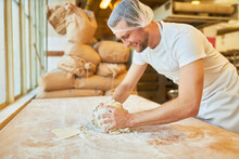Young Man As A Baker In Training Kneading The Dough