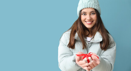 Wall Mural - Young woman in warm gloves with gift box on blue background