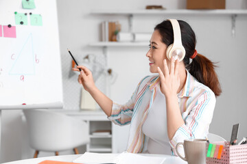 Canvas Print - Young Asian tutor in headphones giving Math lesson at home