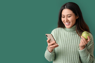 Sticker - Beautiful young Asian woman with mobile phone and apple on green background