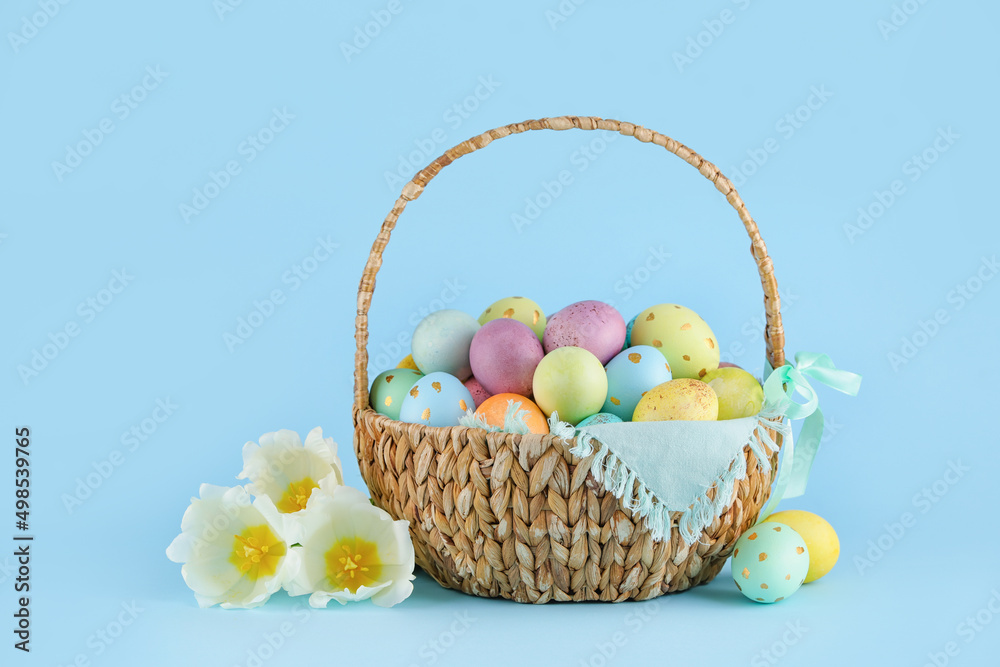 Wicker basket of painted Easter eggs and flowers on blue background