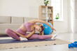 © Studio Romantic - Serious fit woman stretching her body while having a yoga or sports workout at home. Beautiful fit lady doing a seated side bend stretch exercise on a yoga mat placed on a rug in a modern living room