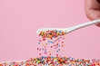 Confectionery sprinkles are sprinkled from a spoon on a pink background. Topping for desserts and pastries. small caramel balls