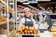 © Dusan Petkovic - A saleswoman holding tray with pastry at supermarket and smiling at the camera.