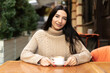 © Andrii Lysenko - Portrait of a smiling woman in a street cafe with a cup of coffee, businesswoman lifestyle, morning breakfast outdoors, urban lifestyle