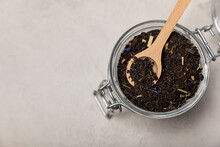 Black Tea In A Wooden Spoon On The Background Of A Glass Jar. Composition On A Light Textural Background. Place For Text.